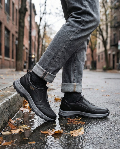 Person wearing black shoes and jeans on a city street with puddles and leaves.
